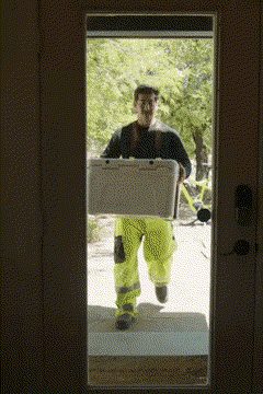 A man carrying a white cooler to a front door