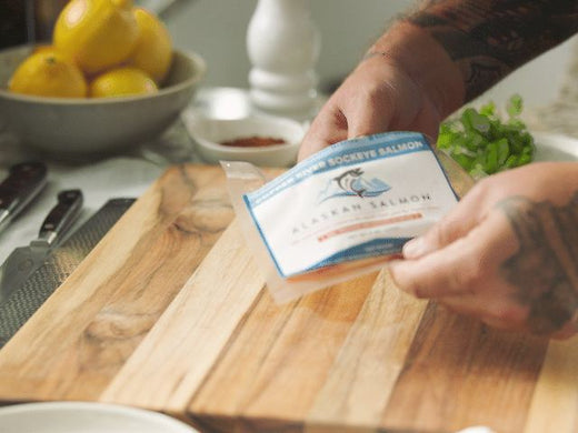 Hands holding a vacuum-sealed sockeye salmon pack over a wooden cutting board in a kitchen