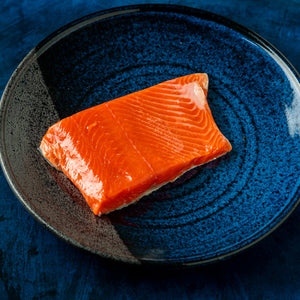 Wild Alaskan sockeye salmon fillet showing vibrant red-orange color and firm texture on a blue ceramic plate