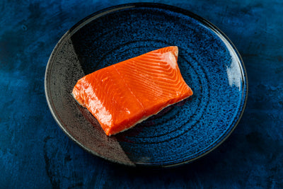 Top-down view of wild Alaskan sockeye salmon fillet showcasing vibrant red-orange flesh with a blue ceramic plate background