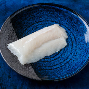 Top-down view of Wild Alaskan black cod (sablefish) fillets, skinless, showcasing glossy raw flesh on a blue ceramic plate