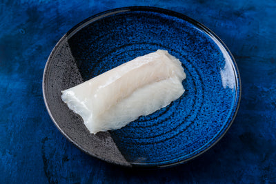 Top-down view of two Wild Alaskan black cod sablefish fillets showing glossy, thick white flesh on a blue ceramic plate